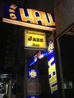 Leuchtreklame des Jazz-Clubs „Die Hall“ bei Nacht mit blau-gelben Schildern